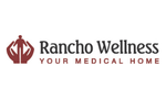 Logo with a maroon symbol resembling stylized hands or a geometric emblem to the left of the text 'Rancho Wellness' in dark lettering, followed by the tagline 'Your Medical Home' underneath.