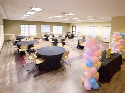 Meeting space at Central Park decorated for small party with multiple round tables with black tablecloths and pink and blue balloon arches. 
