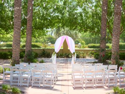 Outdoor space at Central Park set up for a wedding. Multiple white chairs facing an arch covered in pink sheer drapes. Multiple palm trees