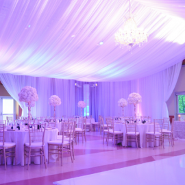 Pink drapes hang from ball room ceiling. Round tables with formal place settings