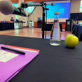 Table with microphone, water, apple, screen in background