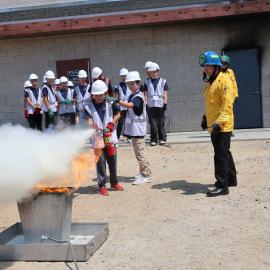 Group of Jr. Firefighters extinguishing a simulated trashcan fire using a fire extinguisher