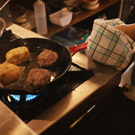 Someone cooking meat in a hot pan over the stove