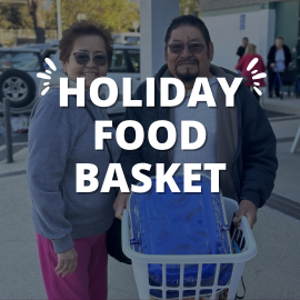 Graphic showing two individuals standing outdoors next to a laundry-style basket filled with a blue-covered container. Large white text in the center reads “Holiday Food Basket,” with decorative accent lines on each side of the word “Holiday.” A parking lot and building are visible in the background. Let me know if you’d like a shorter or more detailed version!